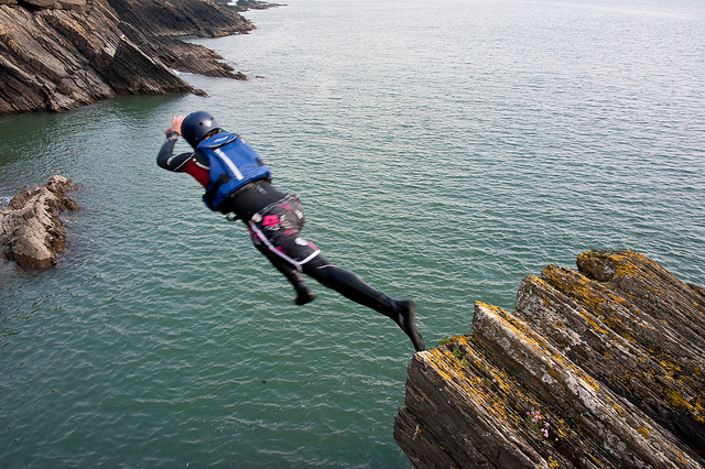 Someone jumping from a cliff ledge into the sea, as part of a coasteering activity