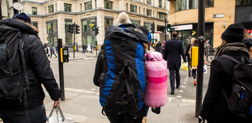 A woman carrying a sleeping bag and a backpack through a crowded street.