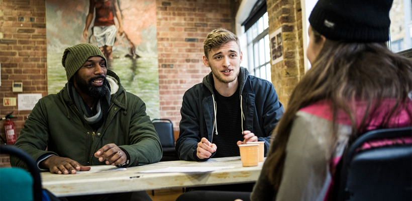 Three people, two men and a woman, talking sat at a table.