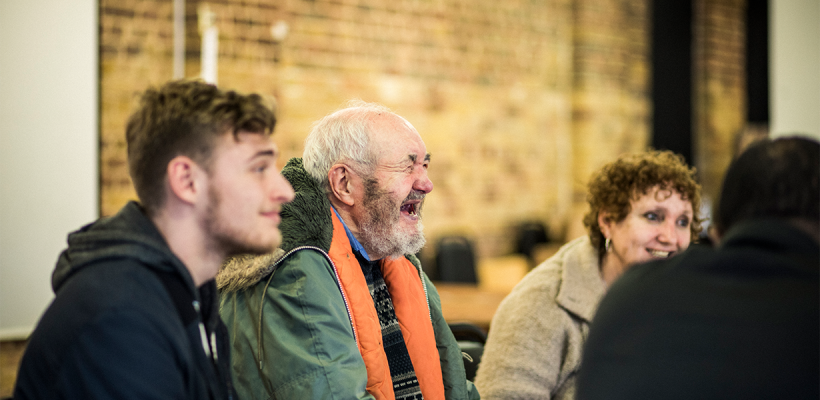 A group of people chatting. An older man is laughing.