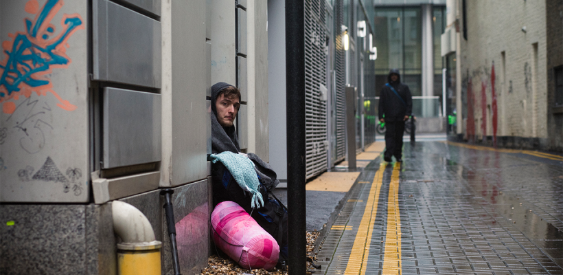 A homeless man sitting in a nook in a street in Brighton.