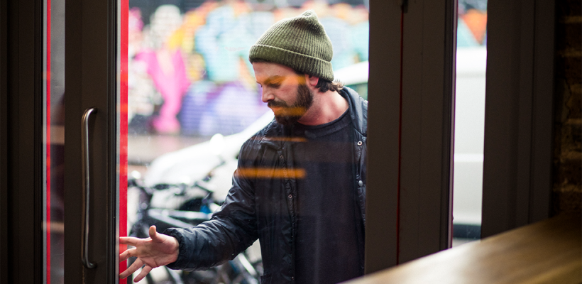 A man pushing open a glass door to enter a building.