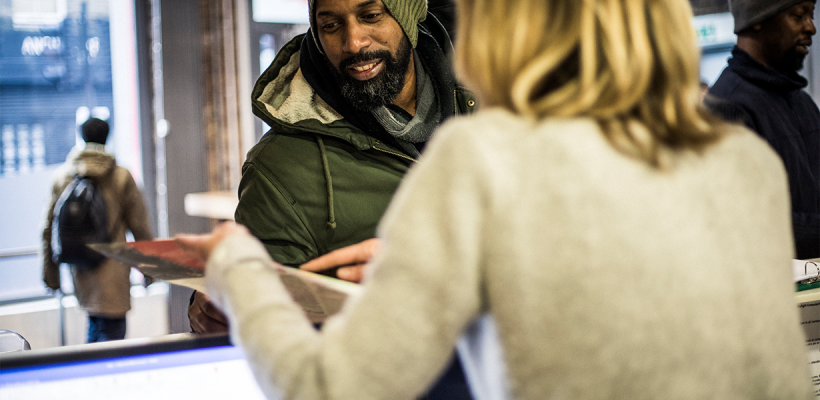 Over the shoulder view of a woman meeting a homeless man arriving at a shelter.