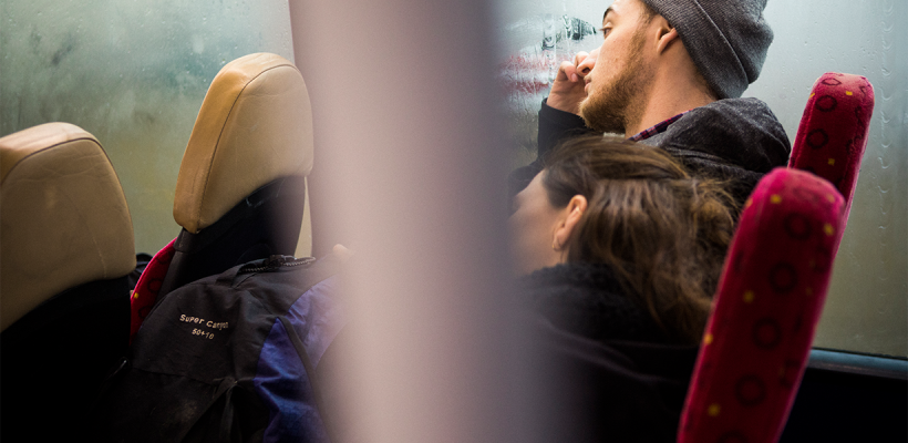 A photo of two people sitting on a bus. The photographer is looking at them from a seat behind.