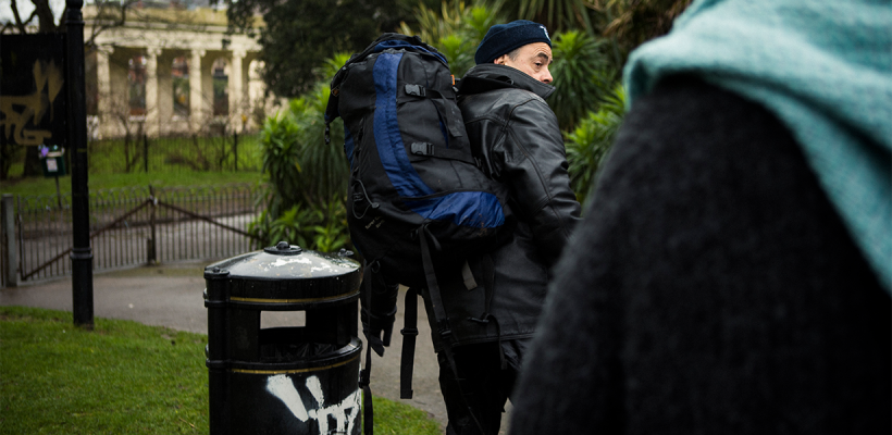 A man with a backpack in a park. He's looking back as if someone called him.