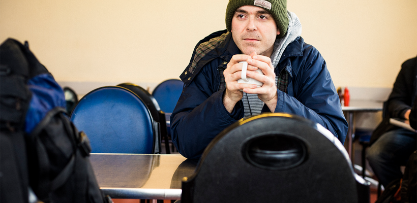 A man with a beanie hat is warming up holding a tea mug.