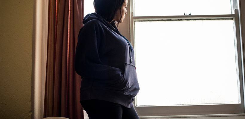 A young woman looking out of a window in her room.