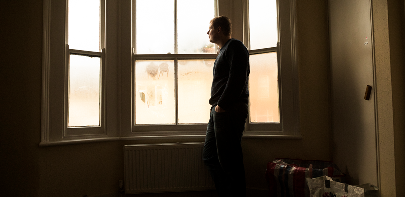 A man stood by a window, looking out.