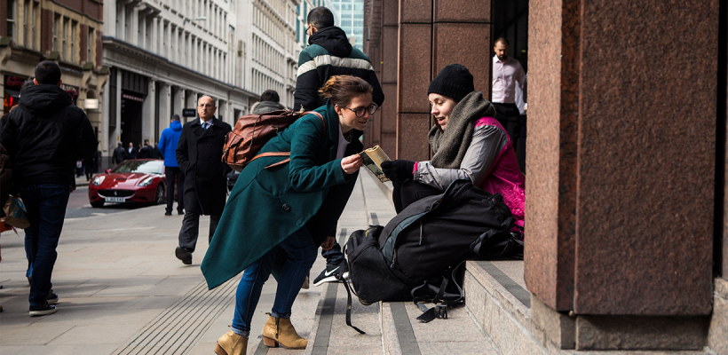 A woman stopping to talk to a homeless girl in a crowded street.